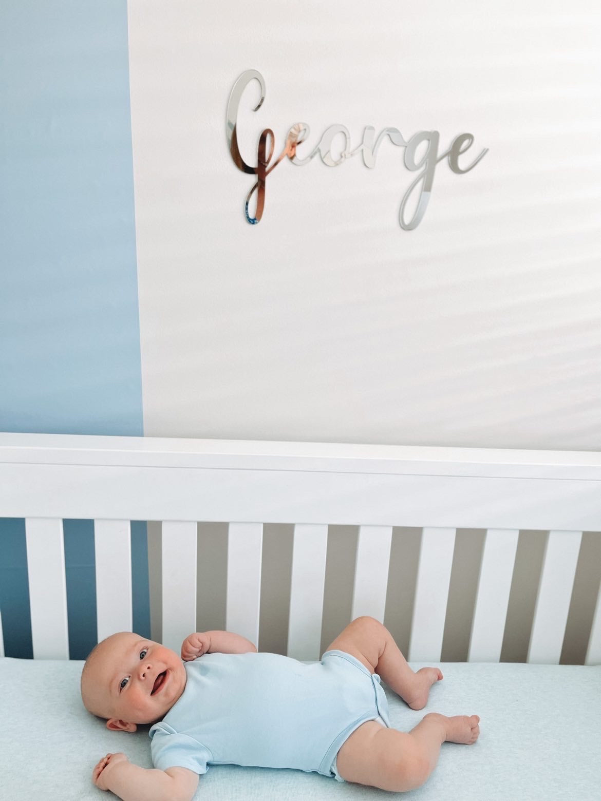 Baby blue arch wall decal creating a soft feature wall in a modern nursery with baby in cot and name sign on wall
