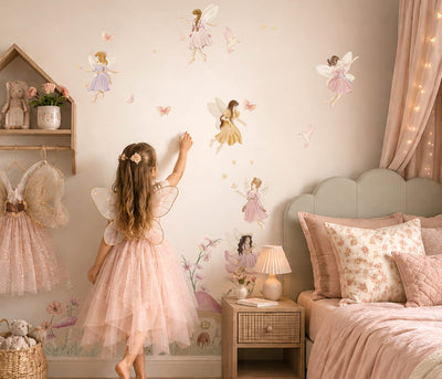 A young girl in a pink fairy costume stands in a cozy, fairy-themed bedroom, touching a wall decorated with large fairy decals. The room features a matching pink bed, a wooden nightstand, a small house shelf with fairy dresses, and warm fairy lights.