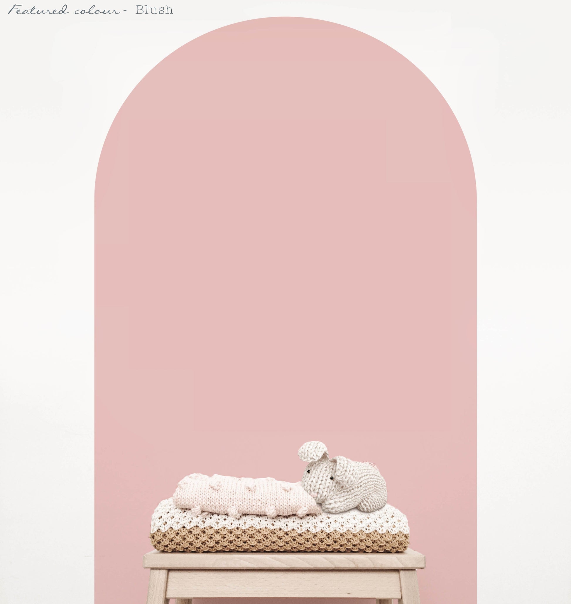 Blush pink arch wall decal creating a warm feature wall in a room with nursery decor on natural wood stool
