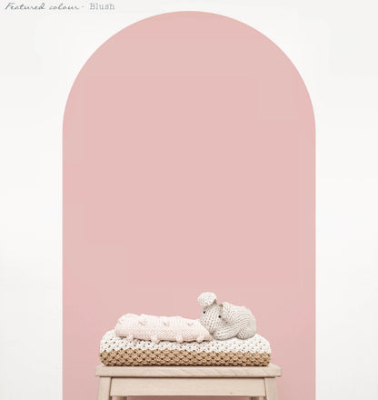 Blush pink arch wall decal creating a warm feature wall in a room with nursery decor on natural wood stool